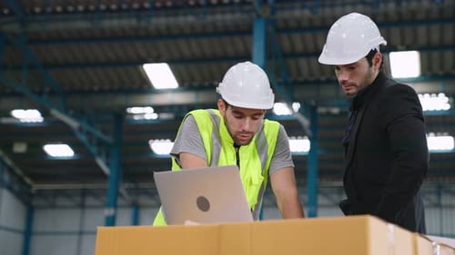 Two Factory Workers Working and Discussing Manufacturing Plan in the Factory