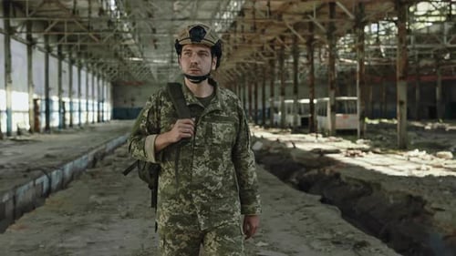 Homme portant un casque et un uniforme militaire marchant sur une ancienne usine