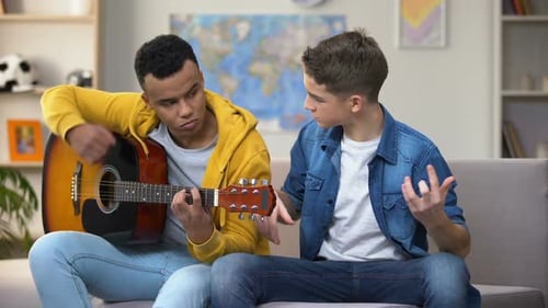 Teen Friends Playing Acoustic Guitar Together Indoors