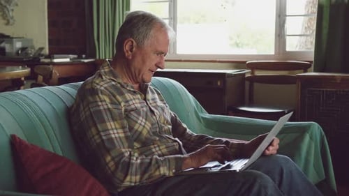 Mature Man Uses Laptop on Couch Indoors