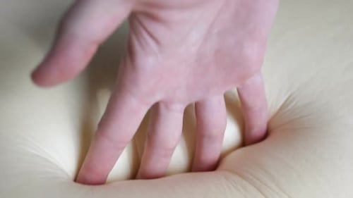 Hand Testing Softness of Beige Cushion