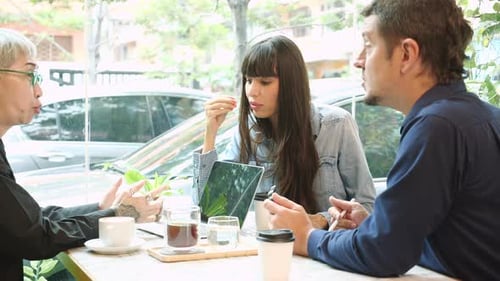 Senior woman talking about agreement of project and explaining with businesspeople in the cafe.