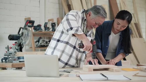Man Teaching Woman to Use Electric Drill in Workshop