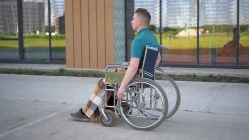 Young Man in a Wheelchair. A Man Rides in a Wheelchair Against the Background of a Glass Building