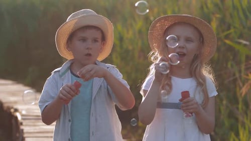 Happy Childhood, Merry Cute Little Girl with Friend Boy in Straw Hats Blow Bubbles and Laugh in