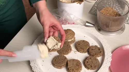 Eine Frau macht einen Kekskuchen. Trägt Buttercreme auf die Werkstücke auf. Gesamtplan