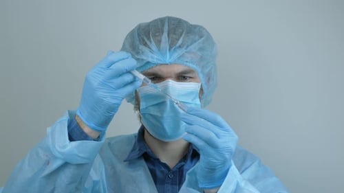 Male doctor holding tube with coronavirus vaccine. Doctor preparing syringe for injection