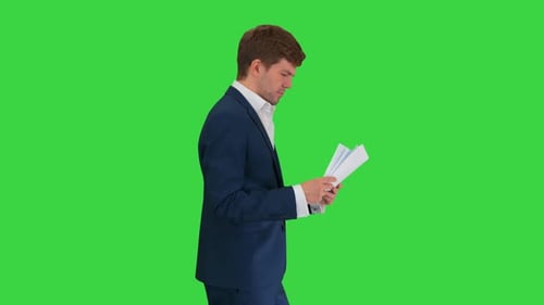 Serious Businessman Reading Documents or Report While Walking on a Green Screen, Chroma Key.