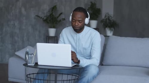 Young Adult Works on Laptop Wearing Headphones Indoors