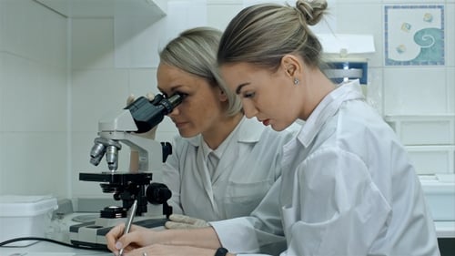 Scientists Observing Sample Under Microscope in Lab