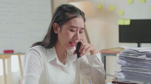 Close Up Of Asian Woman Talking On Phone And Taking Note While Working Hard With Documents At Office
