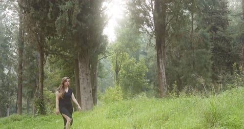 Young beautiful woman with a black dress walking in a green forest