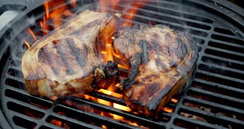 Two Steaks Sizzle on Flaming Grill