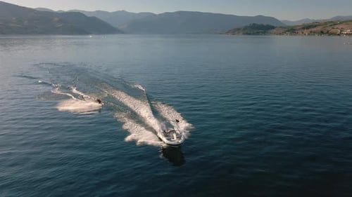 Drone Flying Over Boat Towing Wakeboarder Spraying Water On Sunny Summer Day