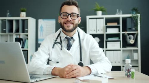 Portrait of Young Doctor Wearing White Gown and Glasses Looking at Camera Smiling