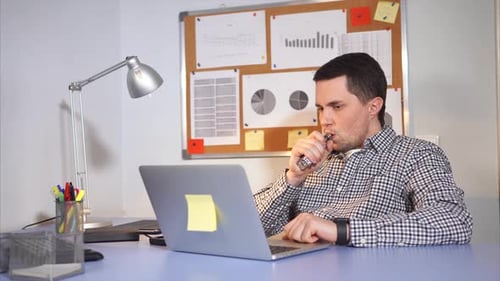 Young Man Smoking an Electronic Cigarette or Vaping in the Office. Young Man Smoking an Electronic Cigarette or Vaping in the Office.