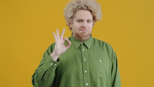 Young Adult Gives OK Hand Gesture on Yellow Background