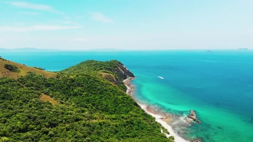 Aerial footage over a green tropical hill with ocean and beach.