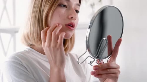 Woman Examining Face in Handheld Mirror
