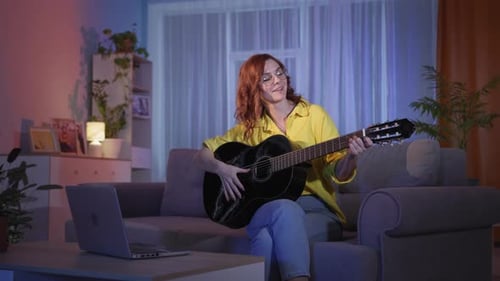 Woman Plays Guitar with Laptop in Living Room