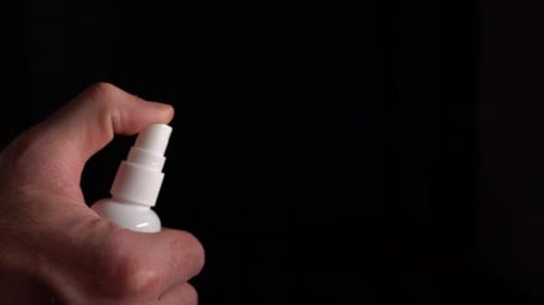 Hand Sprays Bottle Against Black Background
