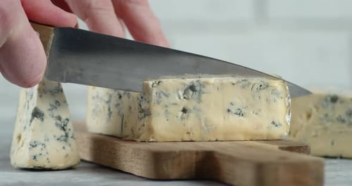 Male Hand with a Knife Cut Off a Piece of Brie Cheese.