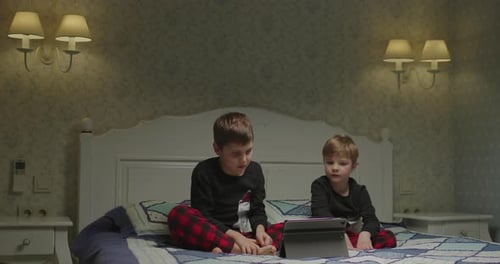 Two Kids Using Tablet Computer on the Bed in Parent Bedroom at the Evening