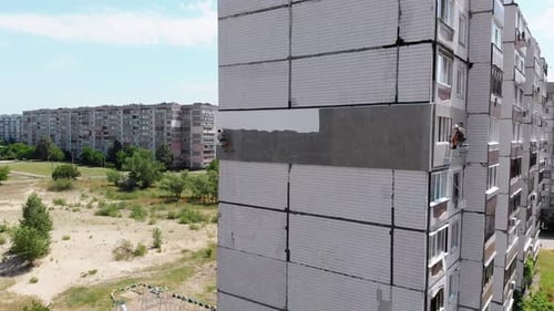 Vista aérea: dois alpinistas industriais realizam trabalhos em edifícios de fachadas de isolamento
