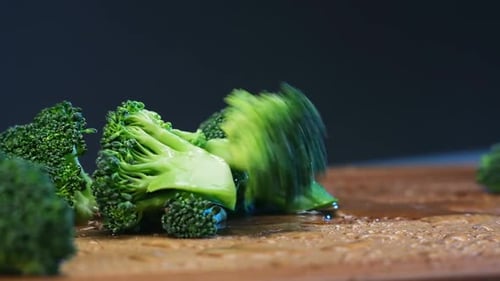 Fresh Green Broccoli Pieces with Water Drops Fall on Board