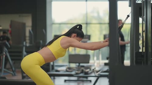 Uma jovem mulher hispânica em um agasalho amarelo realiza um exercício em um crossover puxa uma corda