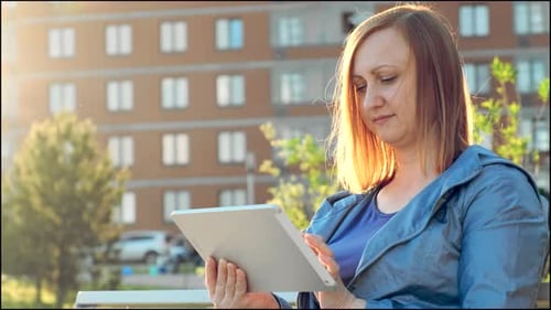 Woman Using Tablet Computer Sitting on Bench in City