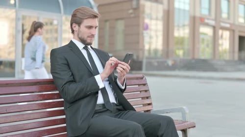Businessman Celebrating Success Using Smartphone on Bench