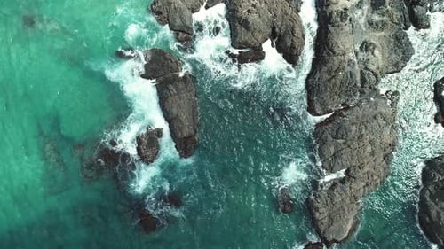 Luftaufnahme von oben auf Meereswellen, die sich in Strandnähe in die Felsen schlagen