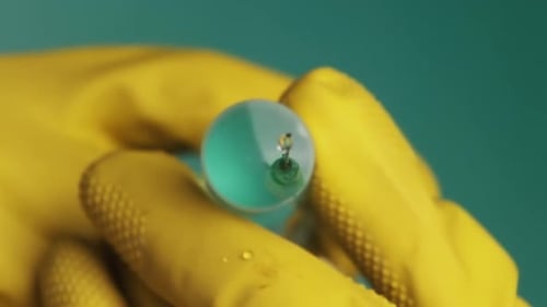 Gloved Hand Holding Syringe With Turquoise Liquid