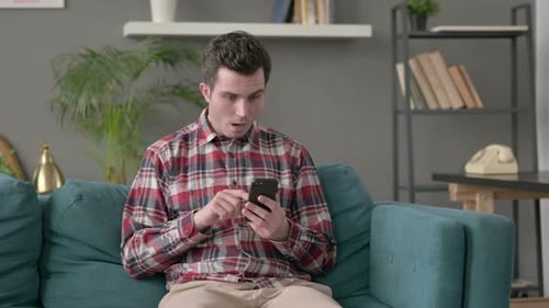 Man Reacts to Phone While Sitting on Couch