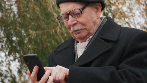 Close-up of a successful senior businessman using a smartphone in the park. Elderly man uses the app