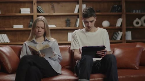 Young Wife Reading Paper Book and Husband Reading Electronic Book on Tablet Computer