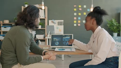 Colleagues Mixed Race Man and Afro-American Woman Talking and Using Laptop in Office