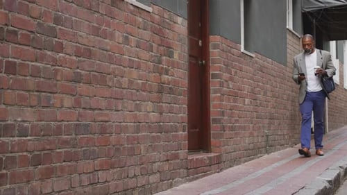 African American man walking in the street and using his phone