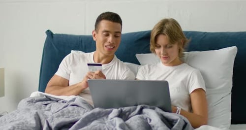 Couple Relaxing in Bed Shopping Online With Laptop