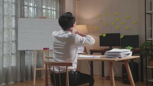Back View Of Asian Man Stretching After Working Hard With Documents At The Office
