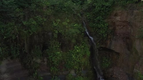 Aerial view slowly flying to a cascade in the tropics with sunbeams from behind the waterfall