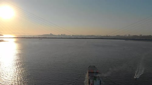 Aerial Shot of a Large Container Ship Moving Into Port Through the Strait with a Big Cable Bridge