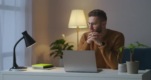 Handsome Man with Glasses Is Sitting Alone at Room in Front of Laptop and Thinking Male Portrait at