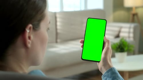 Close Up View of Woman at Modern Room Sitting on a Chair Using Phone With Green Mock-up Screen
