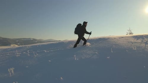 Hiker with Backpack Walking on Snowy Mountain Hillside on Cold Winter Day