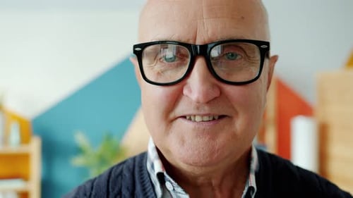 Close-up Portrait of Senior Man in Eyeglasses Smiling Looking at Camera at Home