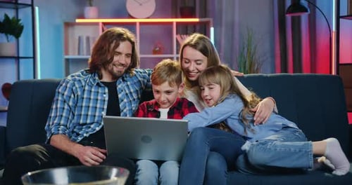 Amorosa pareja con dos hijos que revisa fotos familiares en la computadora mientras pasa el tiempo libre en conjunto