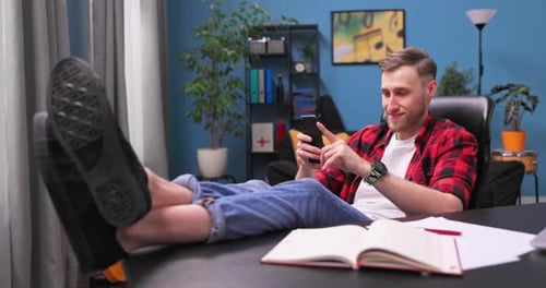 Man Using Smartphone, Feet Up on Desk at Home