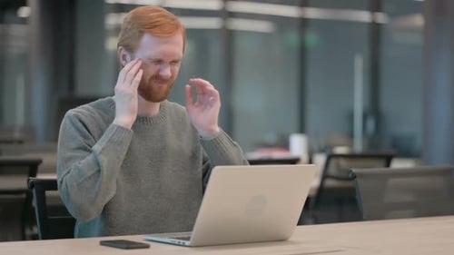 Young Adult Using Laptop Rubbing Temples in Office